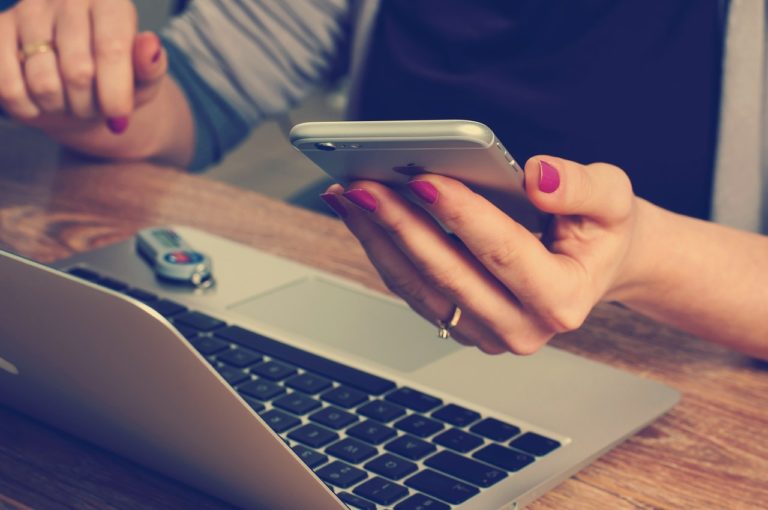 Eine Person, die gleichzeitig am Computer arbeitet und ihr Mobiltelefon überprüft.